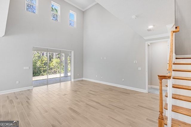 unfurnished living room with light hardwood / wood-style flooring, crown molding, and a high ceiling