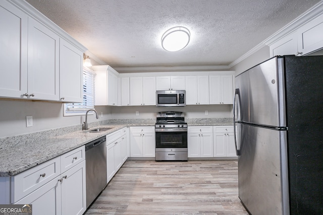 kitchen with light hardwood / wood-style floors, crown molding, sink, stainless steel appliances, and white cabinets