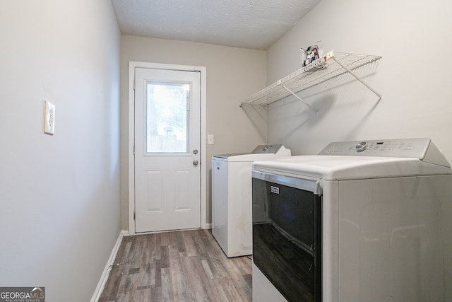 clothes washing area featuring washer and dryer, light hardwood / wood-style flooring, and a textured ceiling