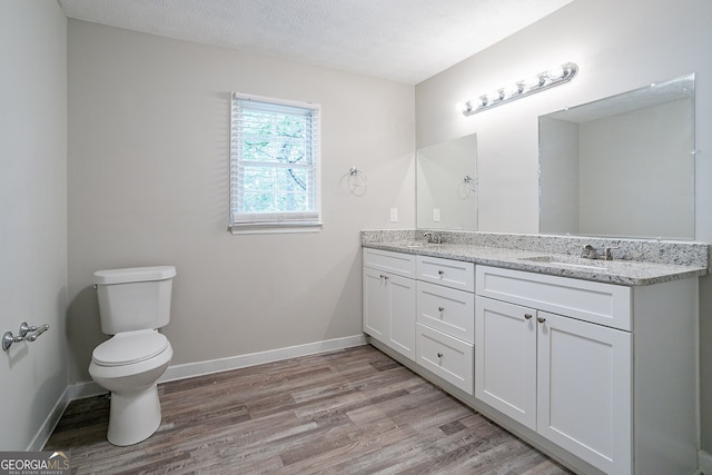 bathroom with toilet, vanity, wood-type flooring, and a textured ceiling