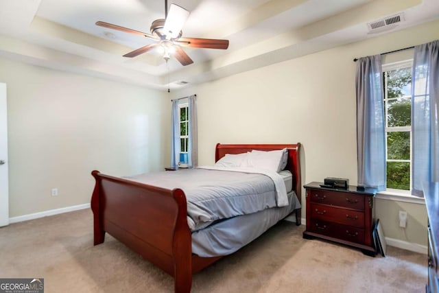 bedroom featuring ceiling fan, multiple windows, and a tray ceiling