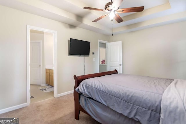 bedroom with light carpet, ceiling fan, ensuite bathroom, and a tray ceiling