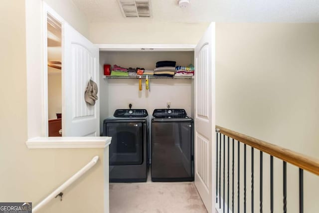 washroom featuring washing machine and clothes dryer, light colored carpet, and a textured ceiling