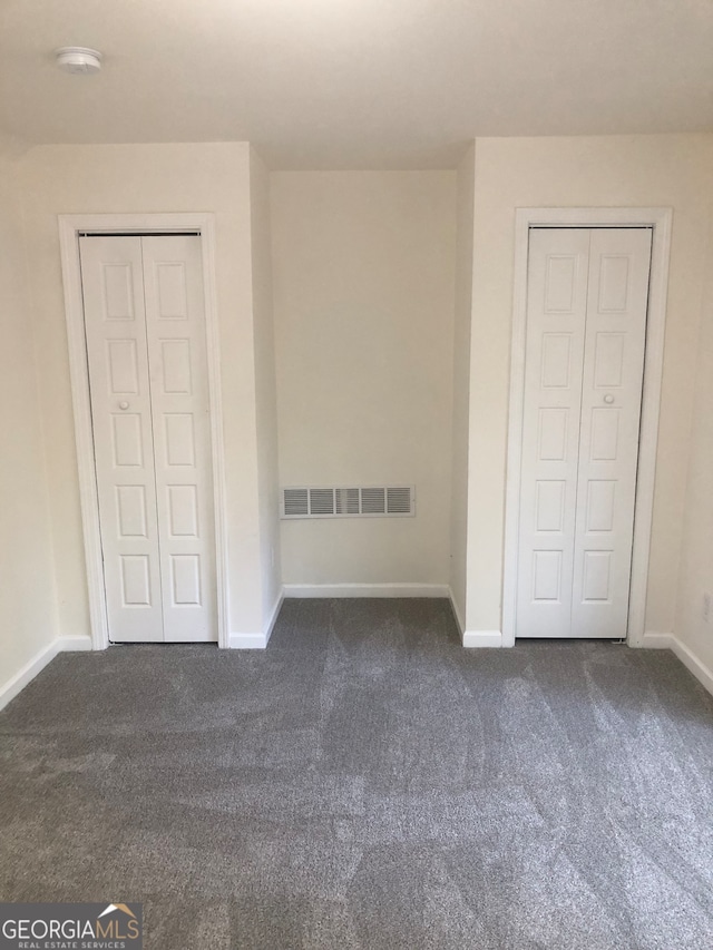 unfurnished bedroom featuring dark colored carpet and two closets