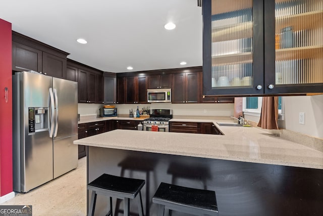 kitchen with kitchen peninsula, dark brown cabinetry, a breakfast bar area, appliances with stainless steel finishes, and sink