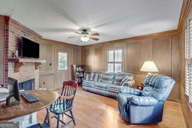 living room featuring ceiling fan, a brick fireplace, light hardwood / wood-style floors, and a textured ceiling