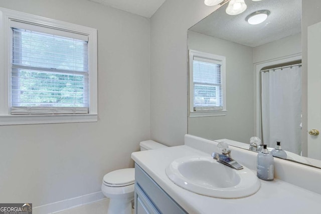 bathroom with a textured ceiling, a wealth of natural light, vanity, and toilet