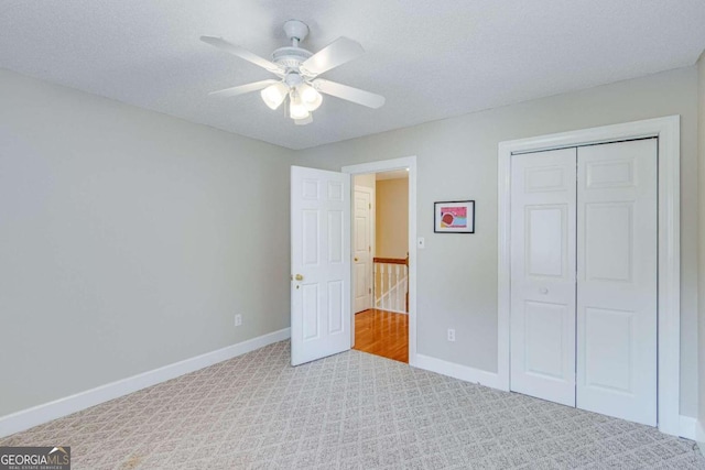 unfurnished bedroom with a closet, light colored carpet, a textured ceiling, and ceiling fan