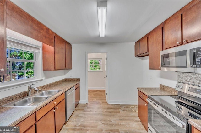 kitchen with brown cabinets, stainless steel appliances, a sink, light wood-style floors, and baseboards