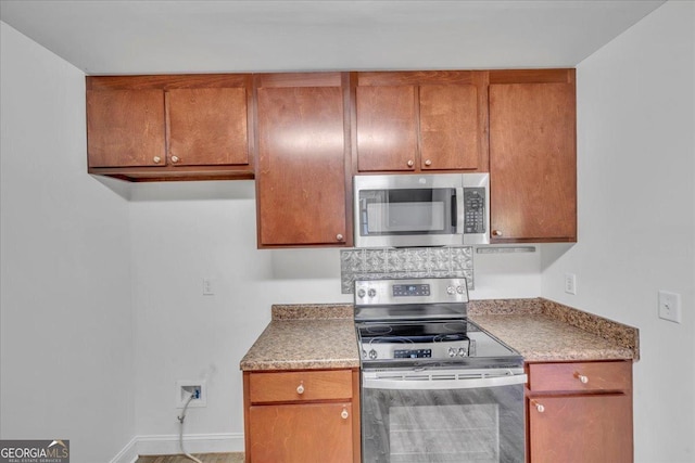 kitchen featuring brown cabinetry, baseboards, appliances with stainless steel finishes, and light countertops