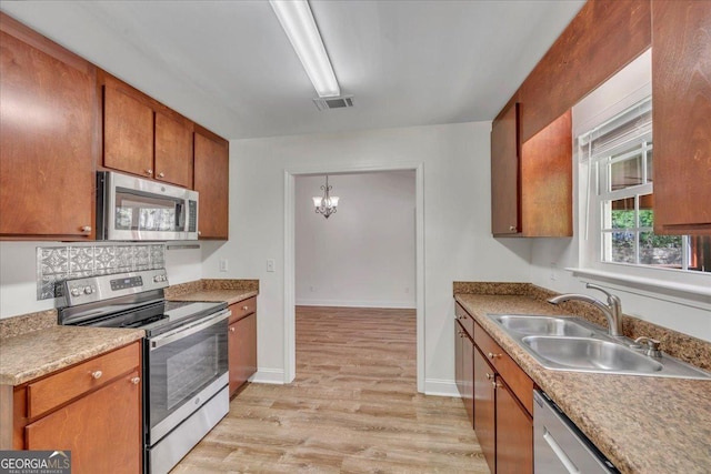 kitchen with a sink, a chandelier, light wood-type flooring, stainless steel appliances, and visible vents