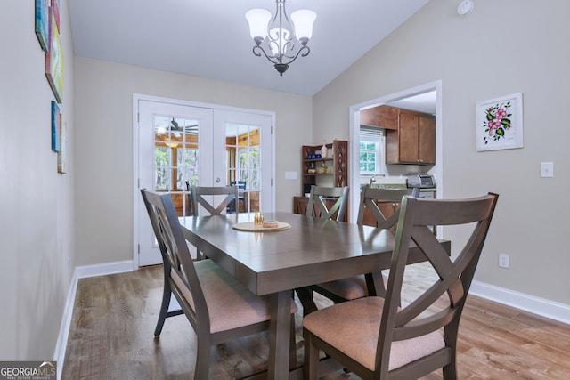 dining area featuring hardwood / wood-style flooring, vaulted ceiling, an inviting chandelier, and french doors