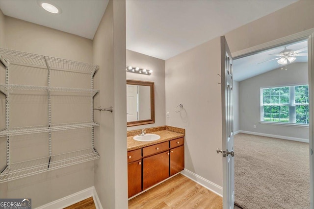 bathroom with vaulted ceiling, wood finished floors, vanity, ceiling fan, and baseboards