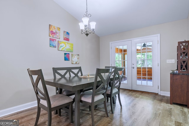 dining area featuring hardwood / wood-style flooring, vaulted ceiling, french doors, and an inviting chandelier