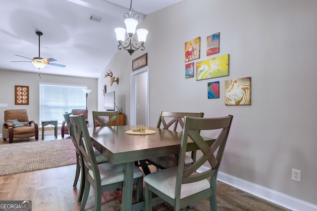 dining space with ceiling fan with notable chandelier, hardwood / wood-style flooring, and vaulted ceiling