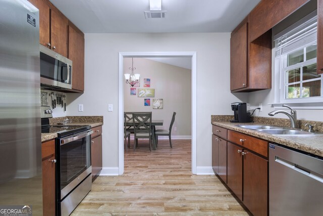 kitchen featuring sink, vaulted ceiling, appliances with stainless steel finishes, an inviting chandelier, and light hardwood / wood-style floors