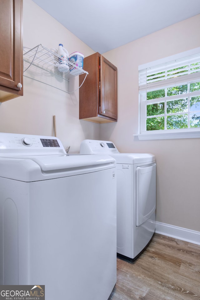 clothes washing area with washer and clothes dryer, cabinets, and light wood-type flooring