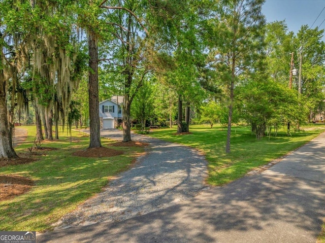 view of community with an attached garage, gravel driveway, and a lawn