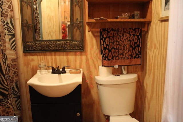 bathroom featuring wooden walls, toilet, and vanity