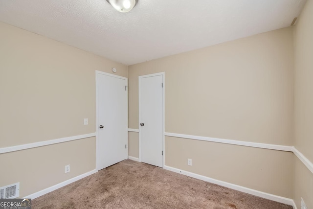 carpeted empty room featuring a textured ceiling, baseboards, and visible vents
