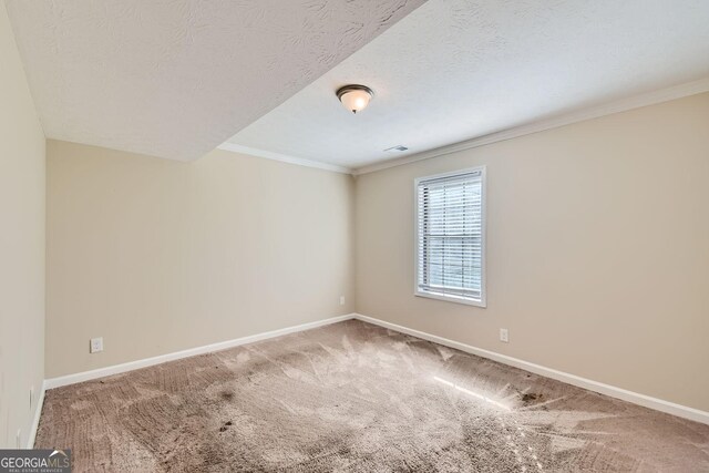 empty room featuring a textured ceiling, crown molding, carpet flooring, and baseboards