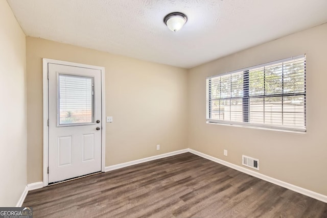 unfurnished room featuring visible vents, baseboards, a textured ceiling, and dark wood-style floors