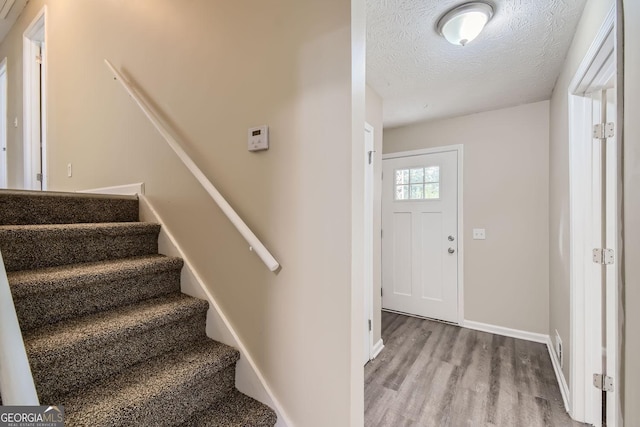 stairs featuring a textured ceiling, wood finished floors, and baseboards