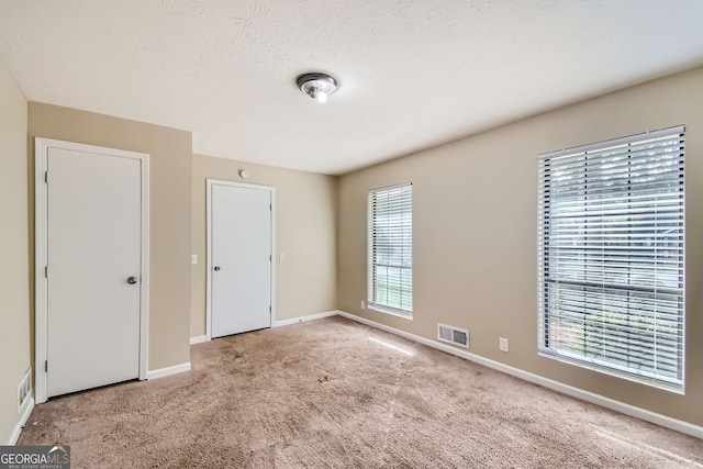 unfurnished bedroom with light carpet, a textured ceiling, and multiple windows