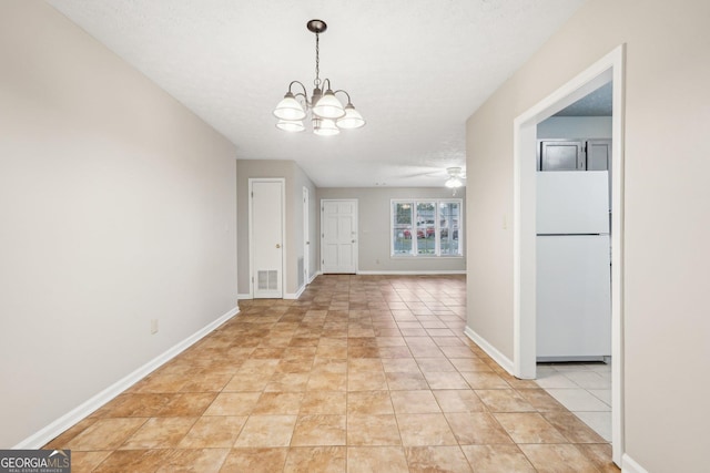 unfurnished dining area featuring a textured ceiling, light tile patterned flooring, ceiling fan with notable chandelier, visible vents, and baseboards