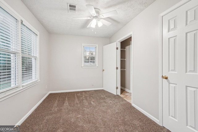 unfurnished bedroom with baseboards, visible vents, carpet, a spacious closet, and a textured ceiling