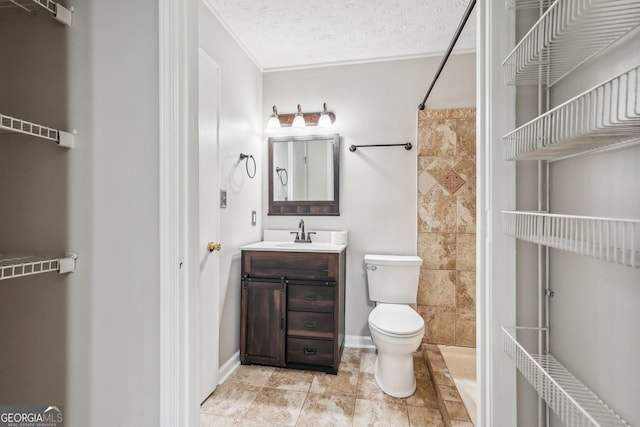 bathroom with toilet, a tile shower, a textured ceiling, vanity, and baseboards