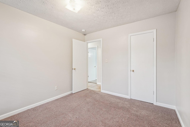 unfurnished bedroom featuring light carpet, a textured ceiling, and baseboards