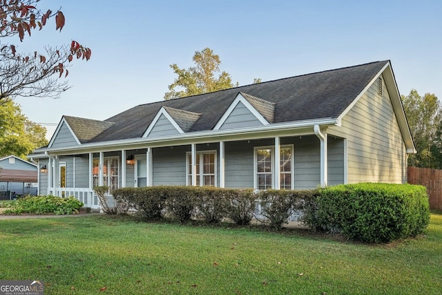 view of front of home with covered porch, roof with shingles, and a front lawn