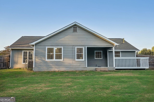 rear view of property with a deck, a yard, a shingled roof, and fence