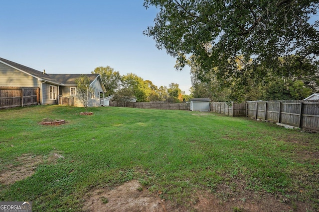 view of yard with an outbuilding, a storage unit, a fire pit, and a fenced backyard