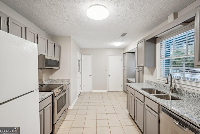 kitchen with light tile patterned floors, visible vents, light stone counters, stainless steel appliances, and a sink