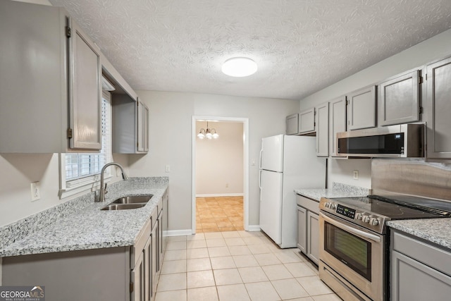 kitchen with appliances with stainless steel finishes, a sink, light stone counters, and gray cabinetry