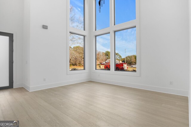 spare room featuring a towering ceiling and light wood-type flooring