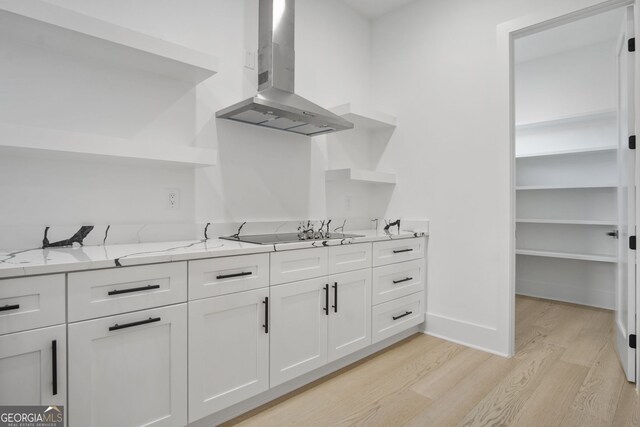 kitchen featuring range hood, white cabinetry, light wood-type flooring, light stone counters, and black electric cooktop