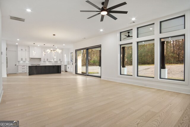 unfurnished living room featuring light hardwood / wood-style floors, plenty of natural light, and ceiling fan with notable chandelier