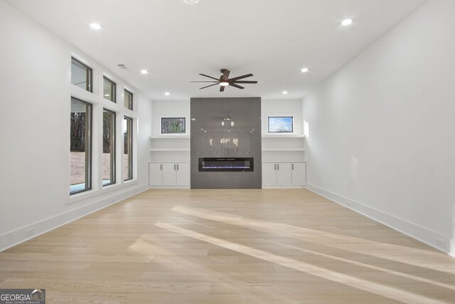 unfurnished living room with light wood-type flooring, a premium fireplace, and ceiling fan