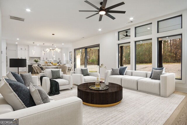 living room with ceiling fan with notable chandelier and light hardwood / wood-style floors