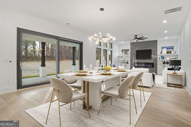 dining area featuring light wood-type flooring, a fireplace, built in features, and ceiling fan with notable chandelier