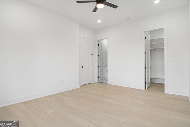 unfurnished bedroom with ceiling fan, a walk in closet, a closet, and light hardwood / wood-style floors