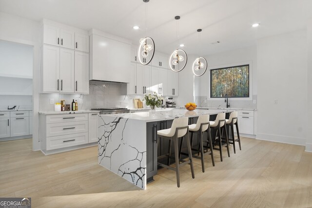 kitchen with white cabinetry, light hardwood / wood-style flooring, a spacious island, and decorative light fixtures