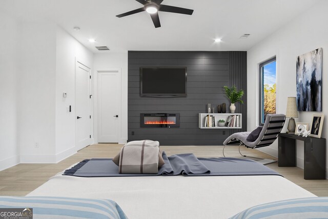 bedroom with ceiling fan, light wood-type flooring, and a large fireplace