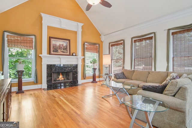 living room featuring ceiling fan, light wood-type flooring, a fireplace, and high vaulted ceiling