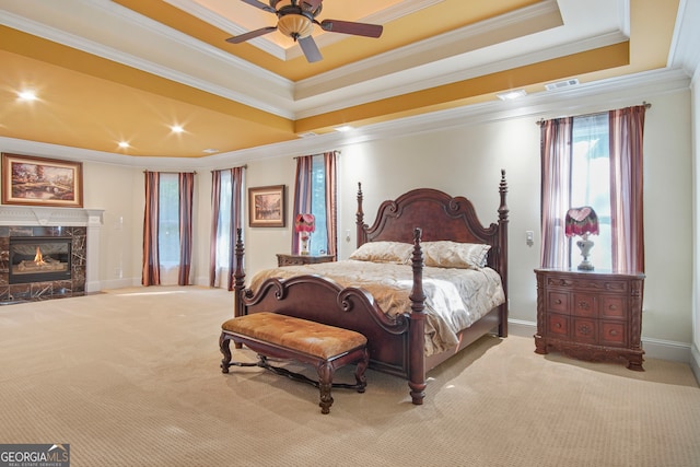 carpeted bedroom featuring a tray ceiling, a high end fireplace, crown molding, and ceiling fan