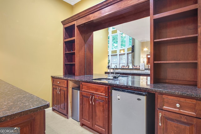 kitchen with light tile patterned flooring, dark stone countertops, stainless steel refrigerator, and sink