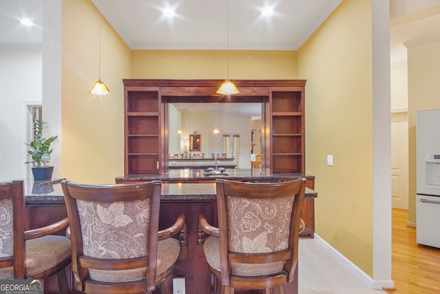 bar featuring crown molding, hanging light fixtures, and light hardwood / wood-style flooring